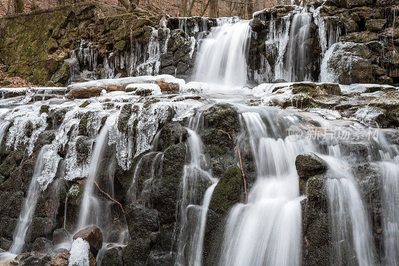 冰柱悬挂在瀑布的一侧，创造了令人惊叹的冬季景色。瀑布位于山区，岩石被冰覆盖。