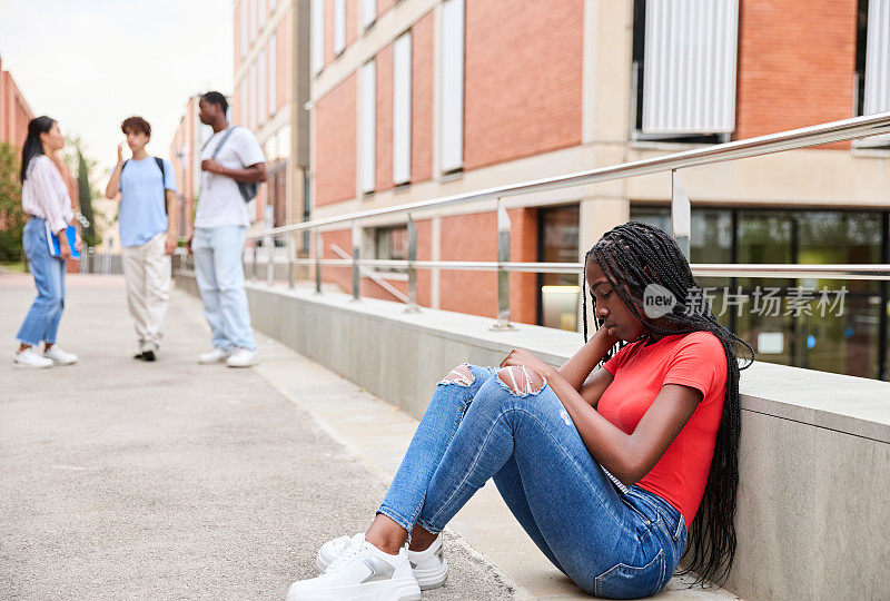 一个十几岁的女学生坐在大学校园的地板上，悲伤而沮丧