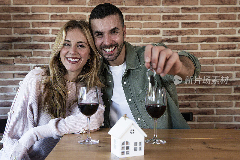 年轻的夫妇庆祝买新房，看着镜头，喝着酒。幸福的男人和女人微笑着拿着公寓的钥匙。