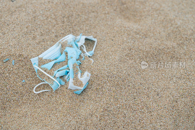 近距离拍摄的天蓝色防护口罩部分埋在沙滩导致塑料污染。人类垃圾处理造成的塑料垃圾对环境的污染。