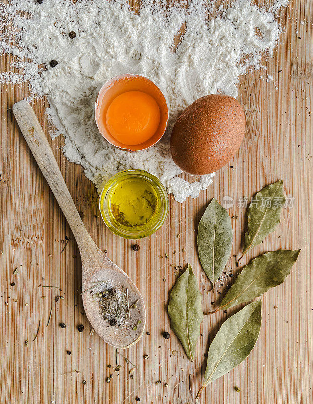 在一个板上有一个完整的鸡蛋，一个带蛋黄的破鸡蛋，面粉，月桂叶，迪尼瓦纳勺子，一个透明的小盘子里的橄榄牛奶和香料。食品摄影
