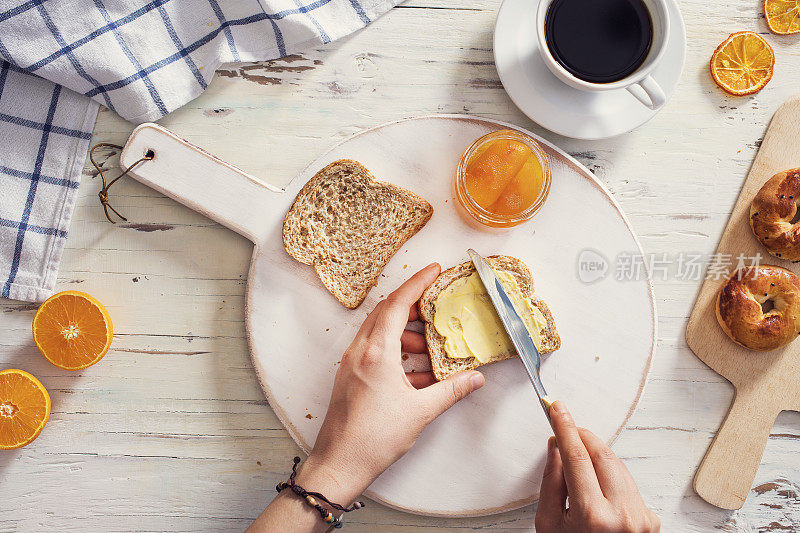 女人用手把黄油涂在切片面包上