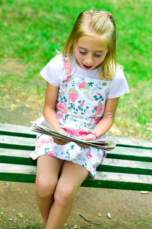 可爱的小女孩坐在长椅上看书