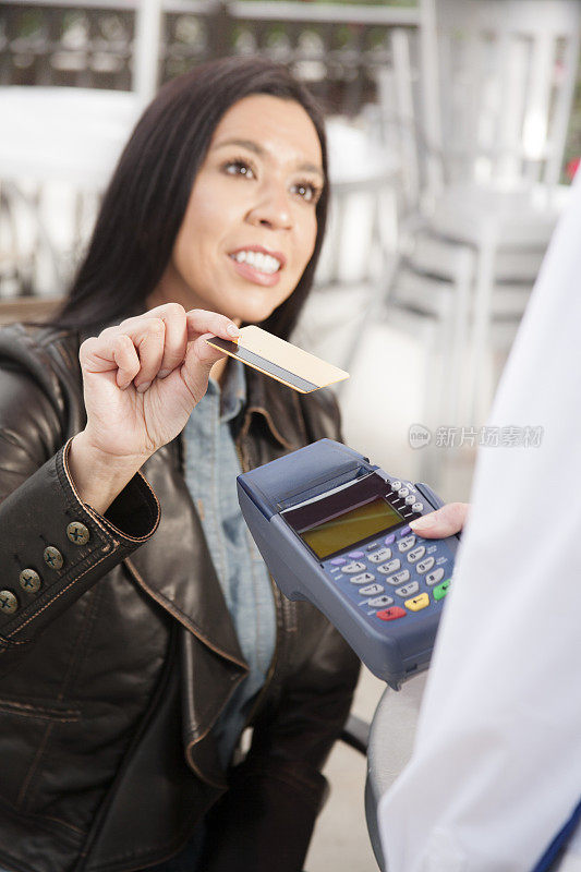 一位女士在户外咖啡馆用信用卡付咖啡钱。