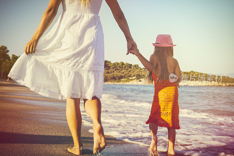 日落时分，母亲和女儿在海滩上牵着手