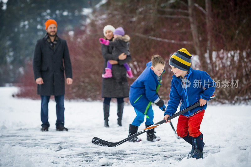 年轻的家庭在外面的雪地里打池塘曲棍球。