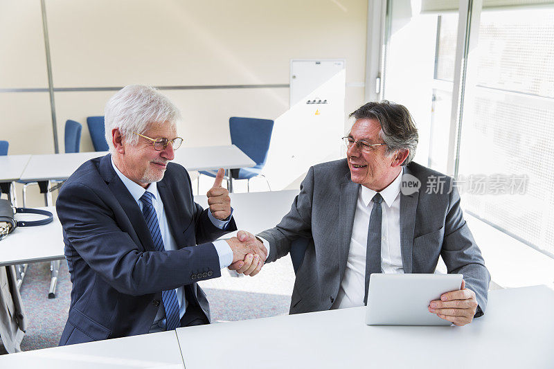 两个商人在他们的办公室握手，竖起大拇指