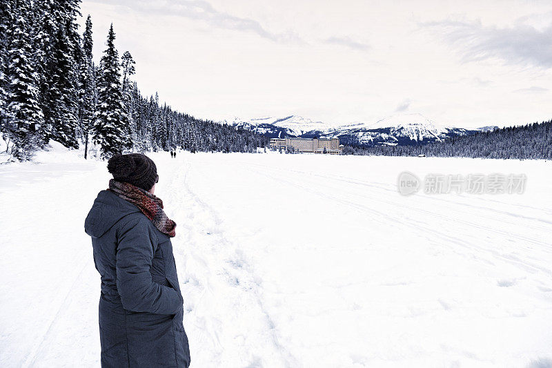 一名穿着冬季服装的白人妇女的侧视图，看着费尔蒙特城堡路易斯湖，班夫国家公园，加拿大阿尔伯塔