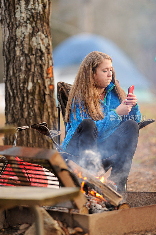 一个女孩在营地的篝火旁用手机