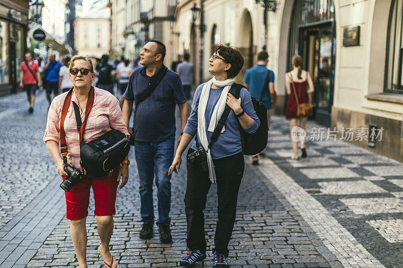 三个朋友走在布拉格老城的一条鹅卵石街上。