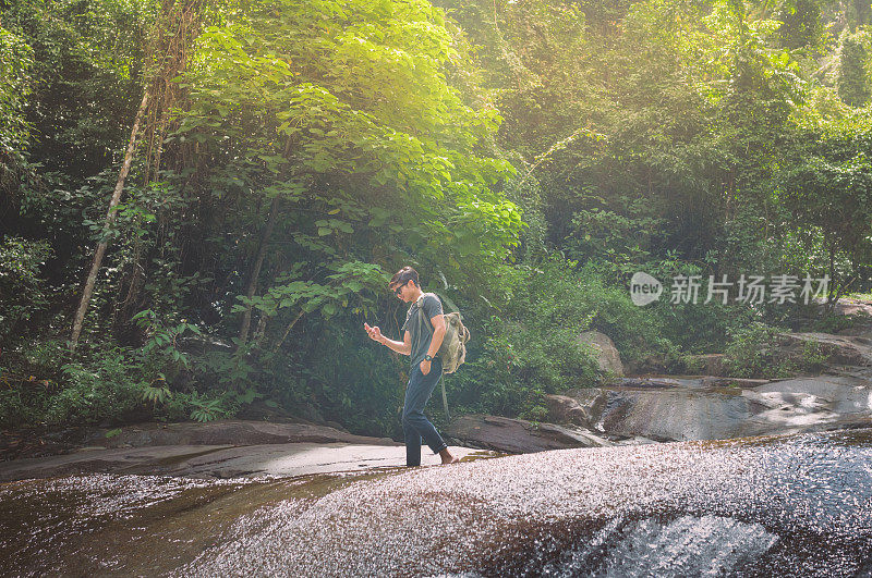 徒步旅行者背包旅行和在线工作与他的手机在瀑布森林。