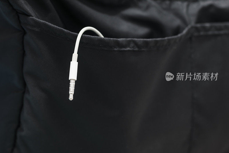 白色耳机插孔皮带挂在一个黑色的包，连接手机，听音乐和歌曲，同时周游世界放松。