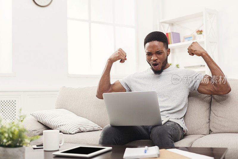 一名年轻黑人举着手提电脑庆祝成功