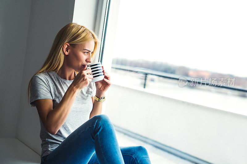 年轻貌美的女人一边喝着咖啡一边透过窗户看外面