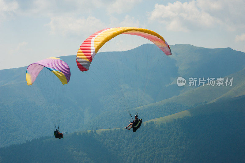 在一个阳光明媚的夏日，两架滑翔伞飞越一个山谷。