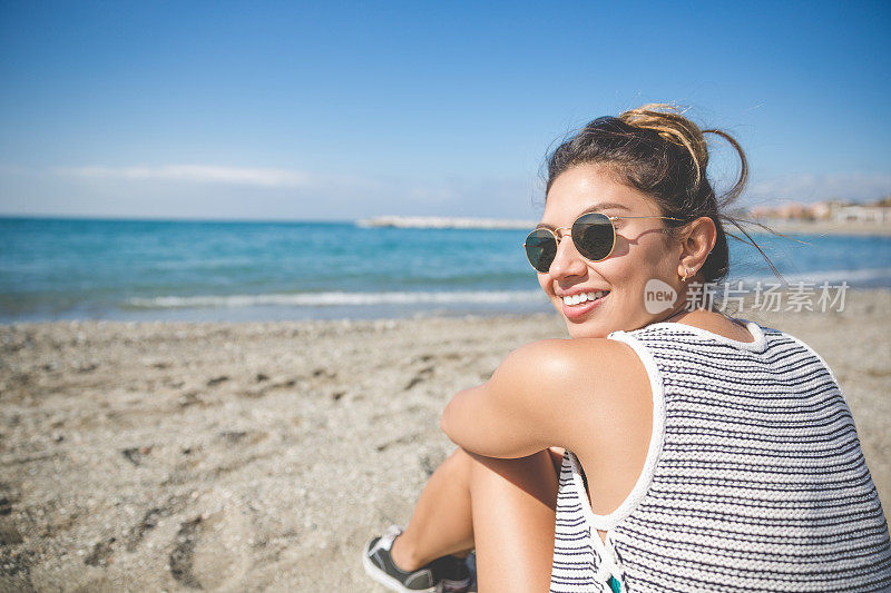 年轻漂亮的女人坐在海滩上微笑