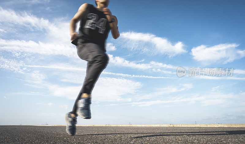 年轻的男运动员在柏油路上迎着天空奔跑