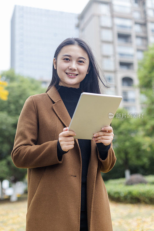 年轻的亚洲女子拿着平板电脑走在街上