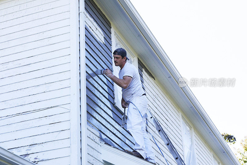 一名男子正在旧房子的外面刷油漆