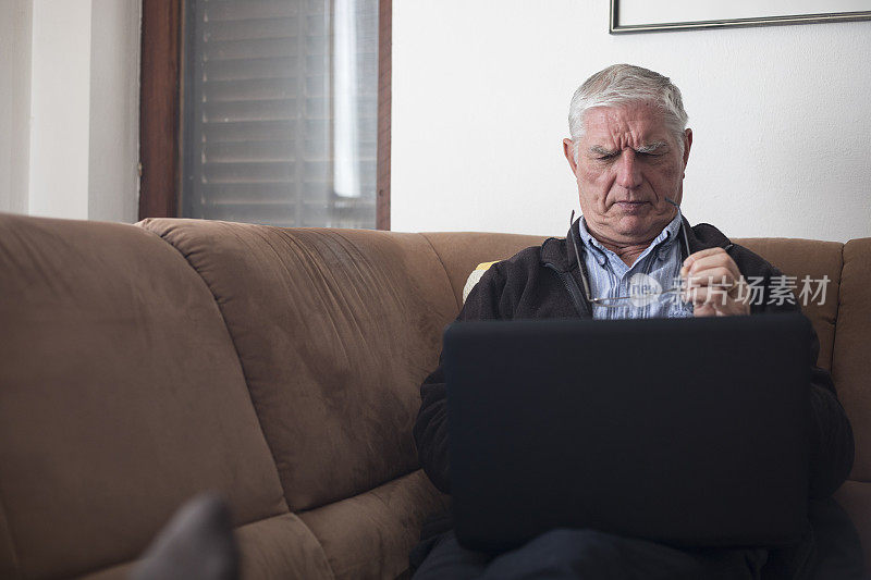 皱眉老人在客厅沙发上使用笔记本电脑