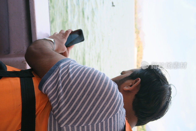 印度拉贾斯坦邦乌代普尔的pichola湖上，一名身穿橙色救生衣的印度男子在摩托艇上用手机自拍，一名游船男子在海边进行水上运动