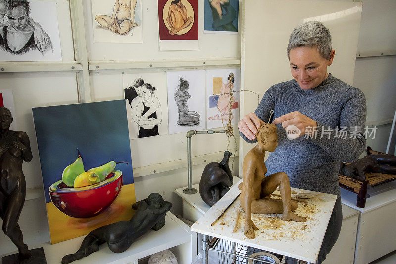 成熟的女性雕塑家在她的工作室里制作她的泥塑。