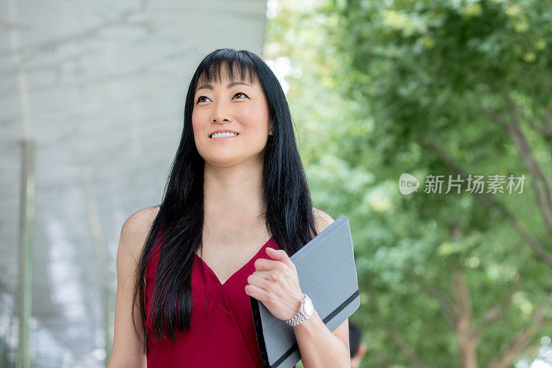 成熟的日本成年女性拿着平板电脑微笑着走在城市里