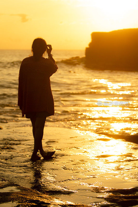 亚洲女人站在海边的海滩在日落