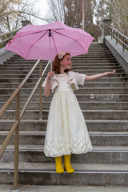 户外楼梯上带着亮色雨伞和靴子的可爱女孩