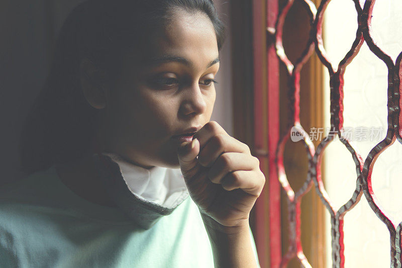 这个悲伤的女孩正在保护自己，戴着口罩，在家里自我隔离。