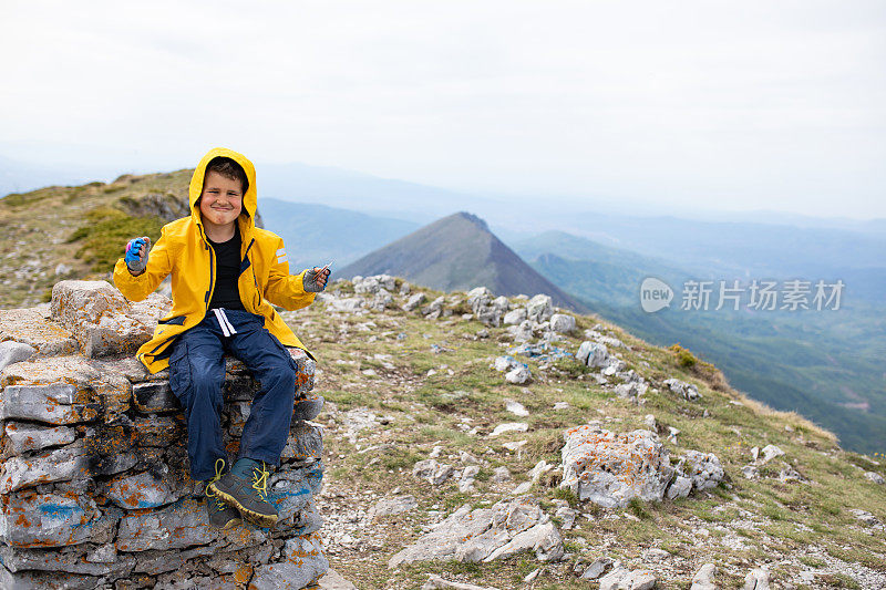 一个可爱的男孩徒步旅行者显示他是多么强壮在山顶