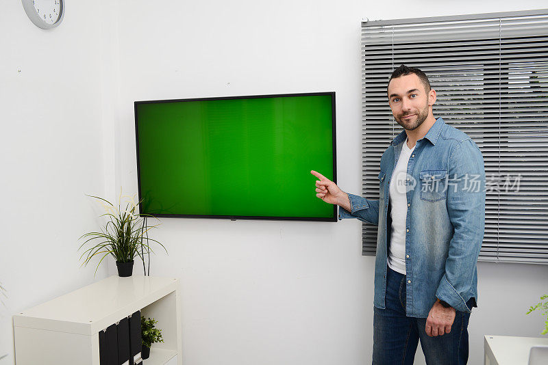 英俊年轻快乐的商人在休闲装商务展示会上站在电视屏幕前，展示绿色的色彩