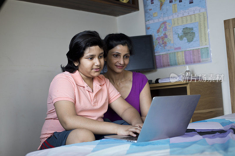 母亲在家里用笔记本电脑帮助儿子在线学习