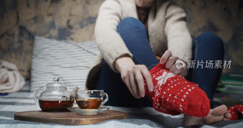 成熟的女人正坐在沙发上喝茶。注重脚上穿的羊毛手工袜子