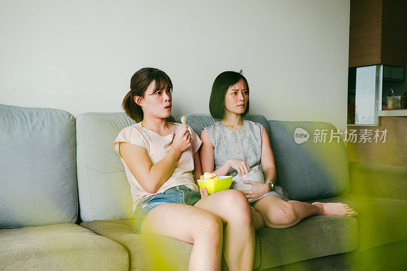 两个美丽的亚洲女人在家看电影。
