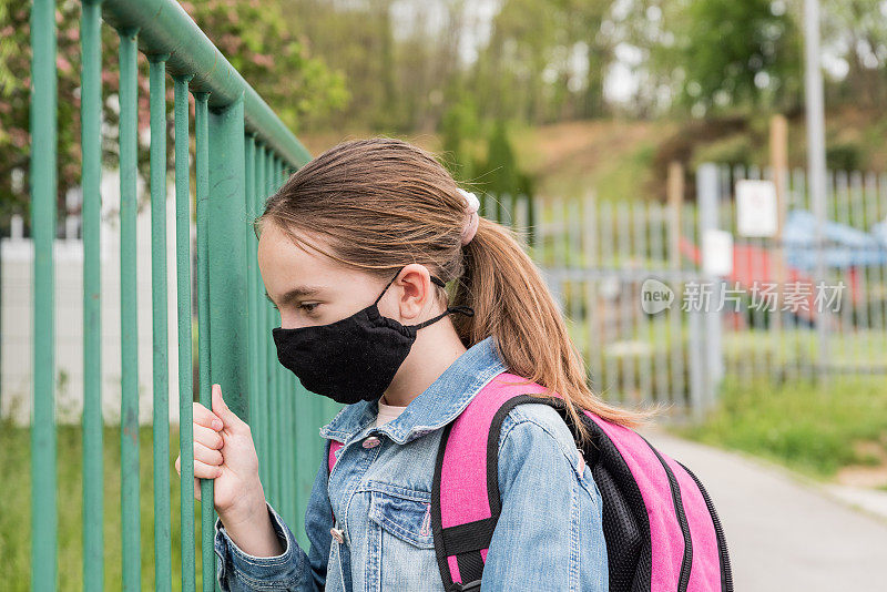 一名戴着口罩的女学生在校门外等待新冠肺炎疫情封锁后重新开放