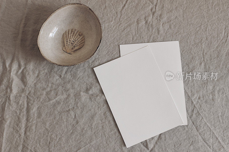 在米色桌子背景上的空白贺卡模型。带有复制空间的现代极简模板。带壳陶瓷碗。品牌标识，展示理念。平铺，俯视图。