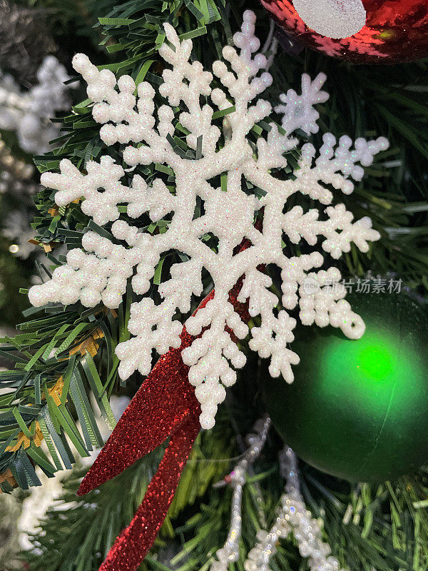 图像白色闪光的雪花饰品挂在人造圣诞树上与绿色塑料云杉针，模糊的白色神仙灯的背景