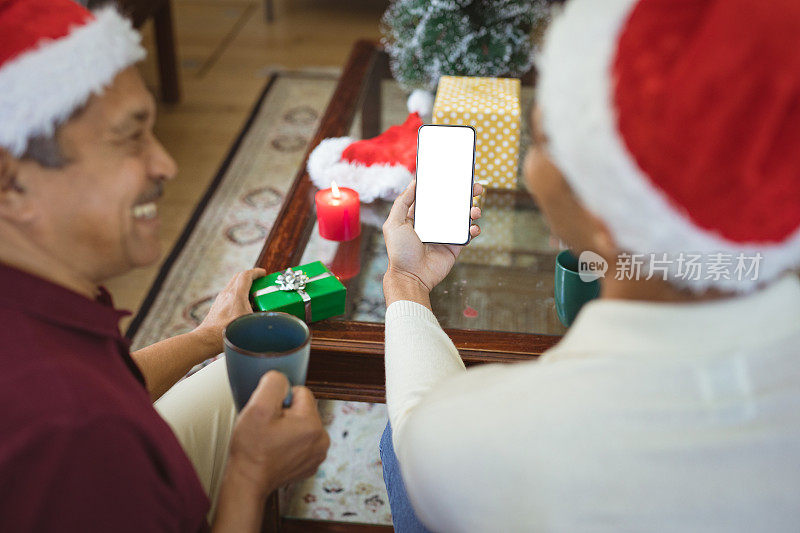 快乐的混血成人儿子和戴着圣诞帽的老人在用智能手机打圣诞视频电话