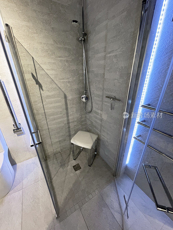现代浴室形象，独立的淋浴间，天然石材墙砖，立方体凳，窗户雨刷和现代定向淋浴头挂在墙上，LED照明