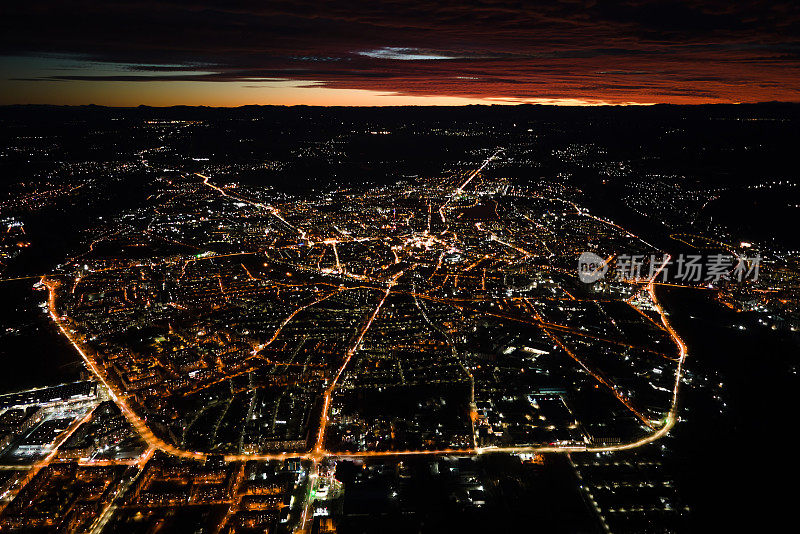 夜间从飞机窗口鸟瞰城市住宅区的建筑物和灯火通明的街道。高海拔地区黑暗的城市景观