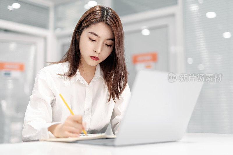 无聊的年轻亚洲女商人在白色房间里用笔记本电脑工作。在办公室工作，工作过度，疲惫，懒惰的员工。