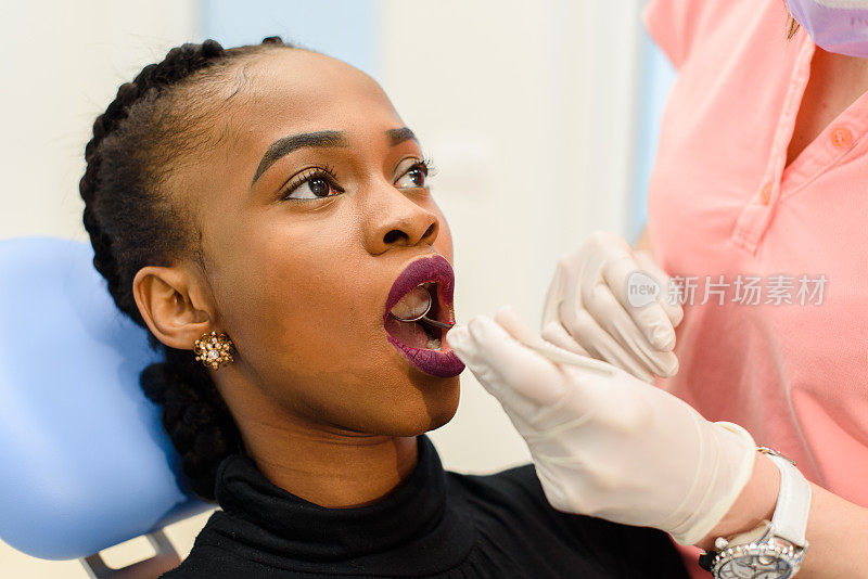 年轻的黑人妇女与女牙医在检查牙齿