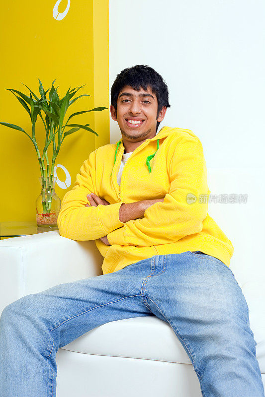 年轻的印度青年愉快的青年坐在沙发上