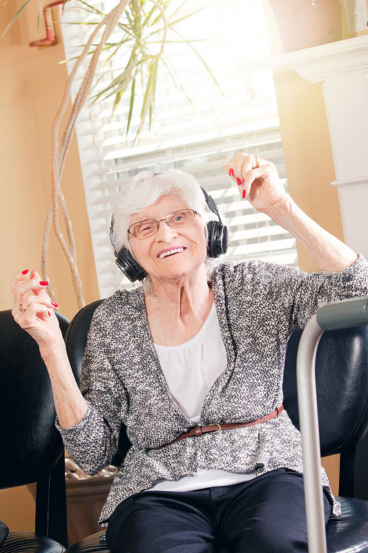 美丽的老妇人通过耳机随着音乐跳舞