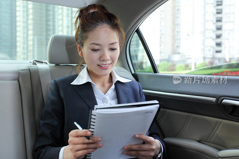 年轻的女商人坐在汽车后座上看文件
