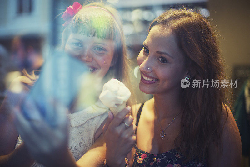 两个年轻女子拿着甜筒冰淇淋在用智能手机自拍