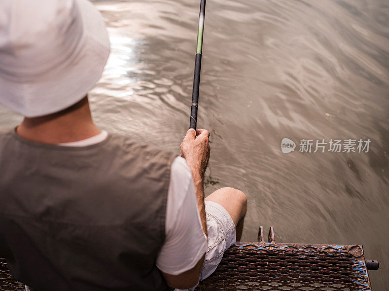 从肩膀上看，一个渔民在码头上捕鱼。