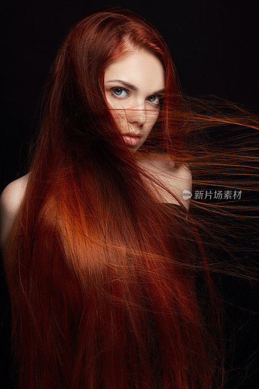 性感漂亮的长头发红发女孩。完美的女人肖像在黑色的背景。漂亮的头发和深邃的眼睛。自然美，清洁皮肤，面部护理和头发。强壮而浓密的头发。花