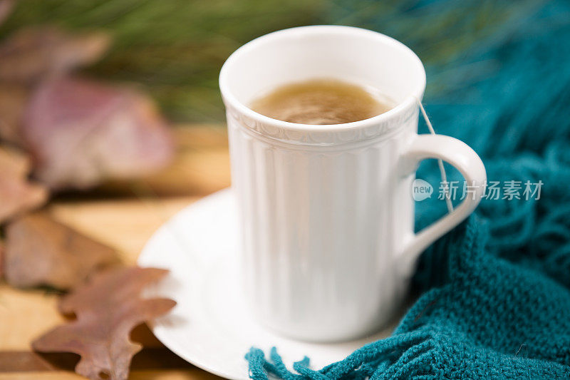 凉茶，白色杯子。秋天的落叶，绿围巾。木制的桌子。